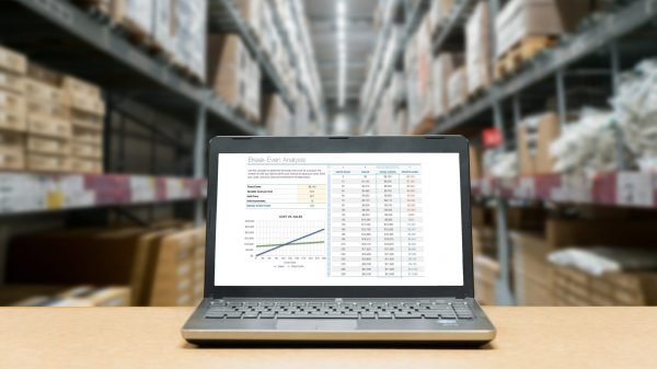 Laptop with analysis sale screen on table with blur warehouse cargo in factory. Smart factory concept.